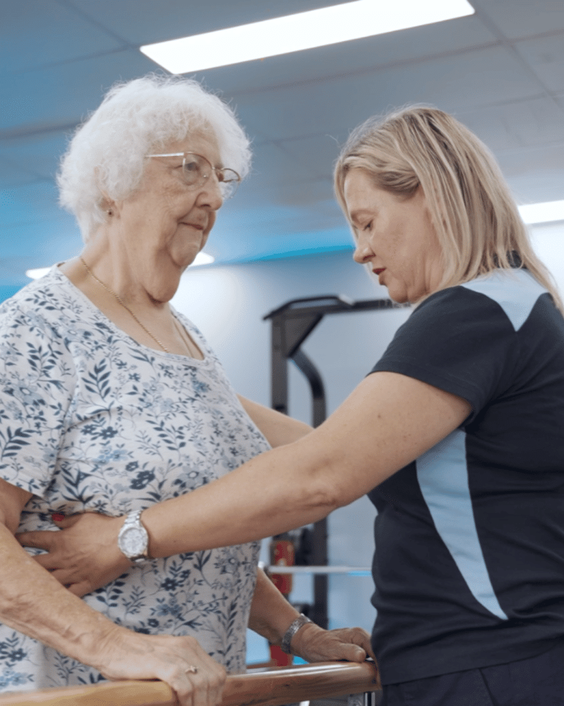 Assist Allied Health physiotherapist assisting an older patient with movement and walking exercises to improve mobility and balance.